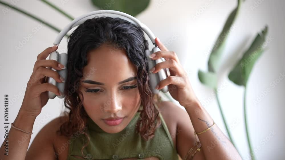 Woman putting on headphones. In a minimalist haven, a girl adorns sleek design headphones, merging style with simplicity. A harmonious blend in the modern sanctuary with a plant in the background.