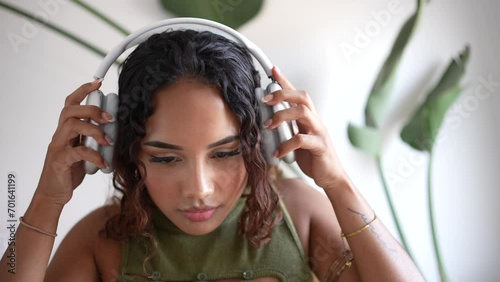Woman putting on headphones. In a minimalist haven, a girl adorns sleek design headphones, merging style with simplicity. A harmonious blend in the modern sanctuary with a plant in the background. photo