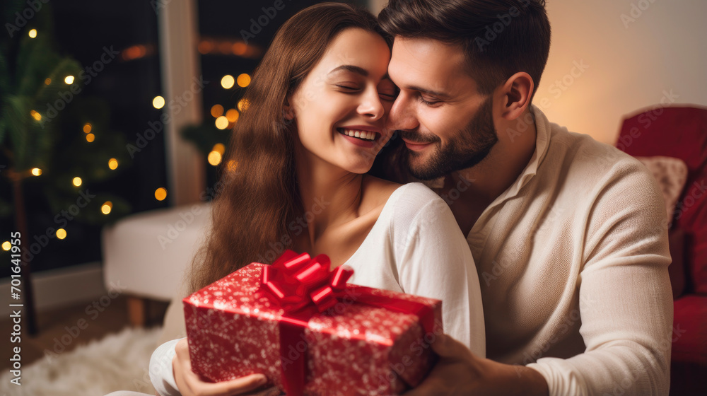 Lovely young couple hugging at home holding gift box, happy giving concept.