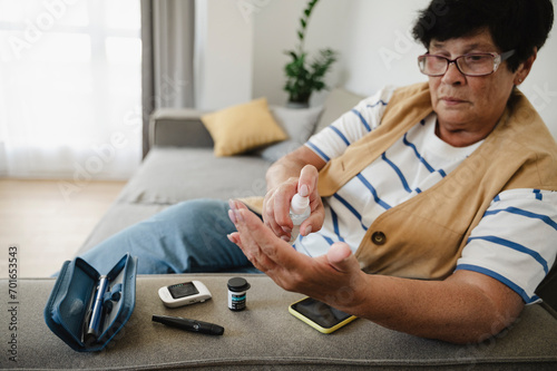 Senior woman using sanitizer for blood sugar testing at home photo