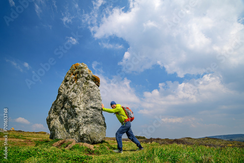 France, Brittany, Hiker pretending to push large menhir along Sentier Cotier route photo