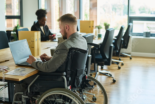 Businessman in wheelchair working on laptop in office photo