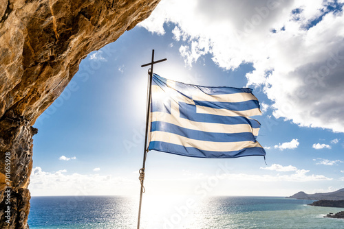 Greece, Crete,Greek flag fluttering against sun shining overMediterranean Sea photo