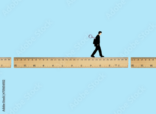 Man walking on broken ruler with wind-up key against blue background