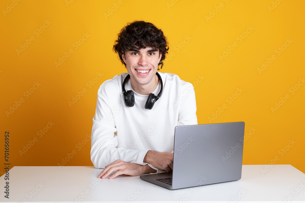 Smiling young businessman with laptop at desk against yellow background Smiling young businessman with laptop at desk against yellow background