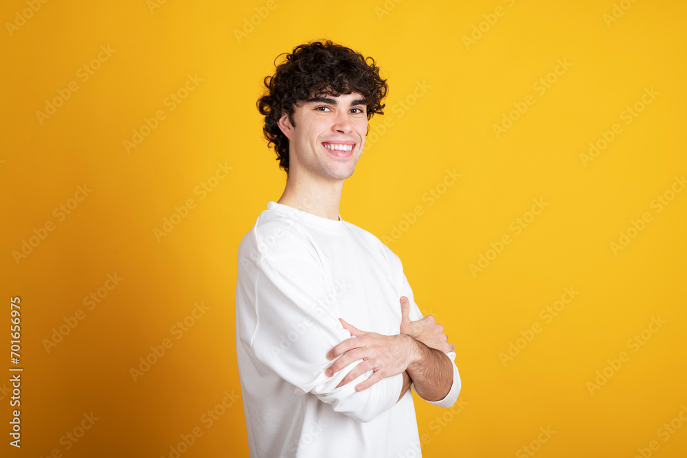 Smiling young man standing with arms crossed against yellow background Smiling young man standing with arms crossed against yellow background