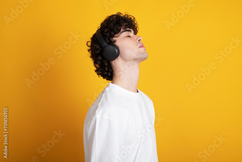 Young man listening to music with eyes closed against yellow background photo