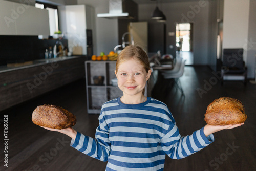 Smiling girl holding baked bread in hands at home photo