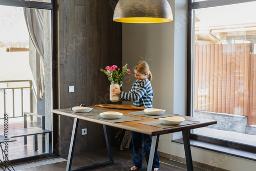 Girl placing flower vase on dining table at home photo