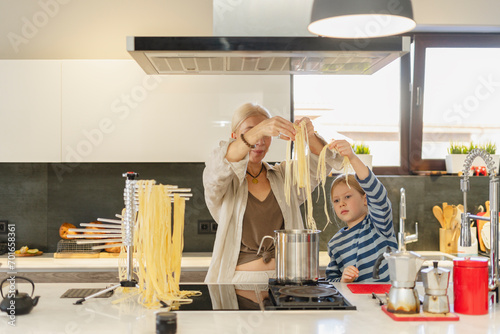 Grandmother and granddaughter boiling spaghetti in cooking pan at home photo