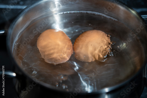Saucepan with two chicken eggs in boiling water on a gas stove, closeup
