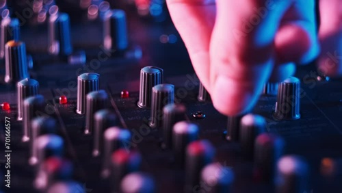 Adjust volume controls on the audio mixer in neon light close-up. Sound engineer moving faders level. Male hand working on mixing console in colorful background. DJ plays music at night club party. 4K