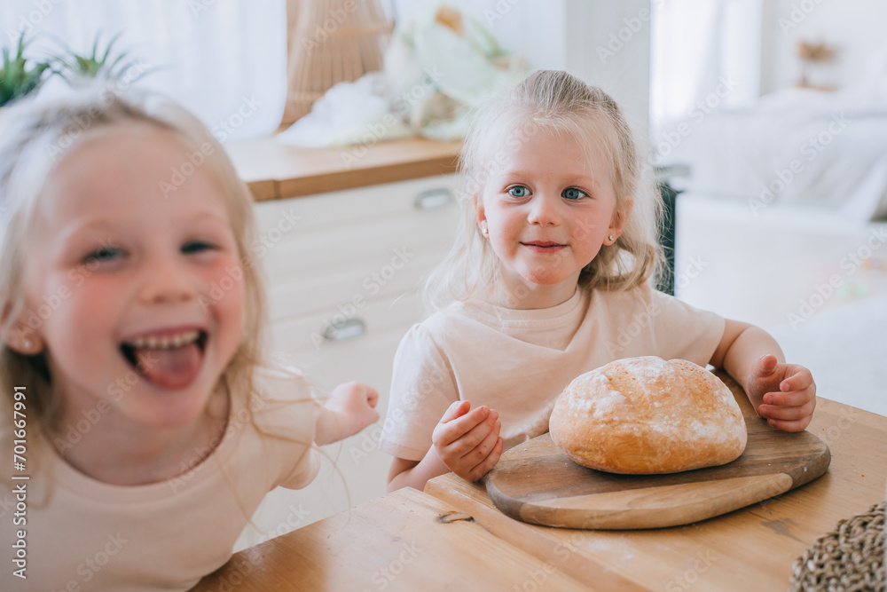Two joyful young sisters with a fresh loaf of bread on a wooden board, laughing and enjoying a moment in a bright, homey kitchen Two joyful young sisters with a fresh loaf of bread on a wooden board, laughing and enjoying a moment in a bright, homey kitchen