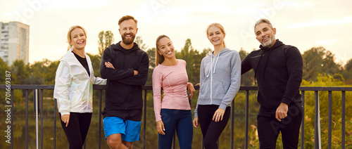 Portrait of a happy sporty people friends in sportswear looking at camera standing in a row on the bridge after successful workout in park. Outdoors training and fitness in nature concept. Banner. photo