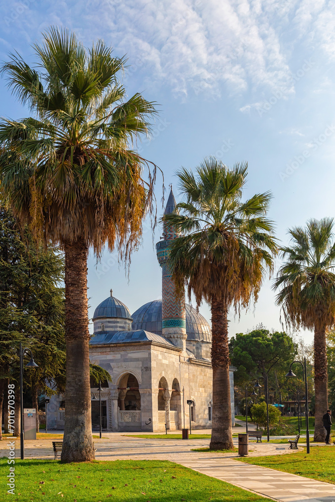 Green mosque (yesil camii) and its turquoise color minaret. Square and park with palm-trees. Nicaea (iznik) in sunny day. Vertical shot. Bursa, Turkey