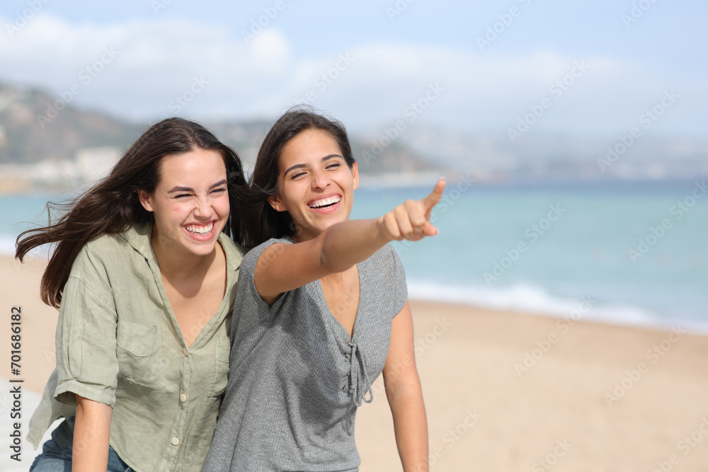 Two friends laughing and pointing away on the beach Two friends laughing and pointing away on the beach