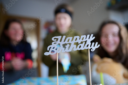Drei unerkennbare Personen vor einem Geburtstagskuchen mit dem Schild "Herzlichen Glückwunsch" im Vordergrund