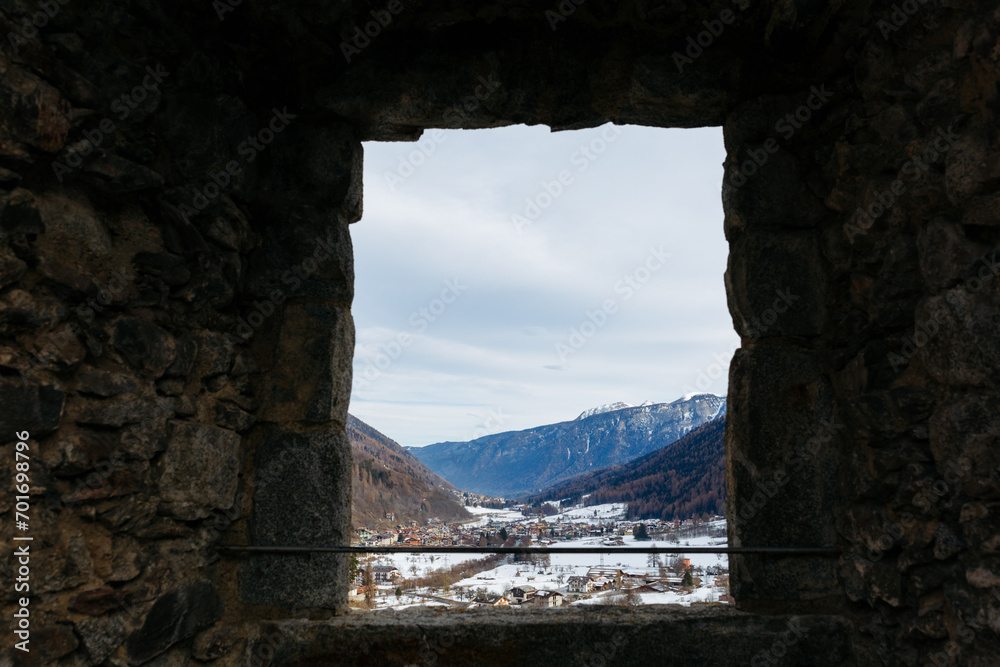 view on snowy mountain range from the window in the old stone wall