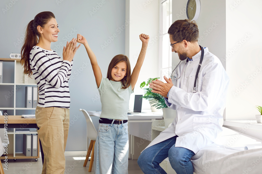 Male pediatrician and happy mother applaud little girl during appointment in medical office. Preteen girl celebrates successful completion of treatment. Medicine, healthcare and pediatry concept. Male pediatrician and happy mother applaud little girl during appointment in medical office. Preteen girl celebrates successful completion of treatment. Medicine, healthcare and pediatry concept.