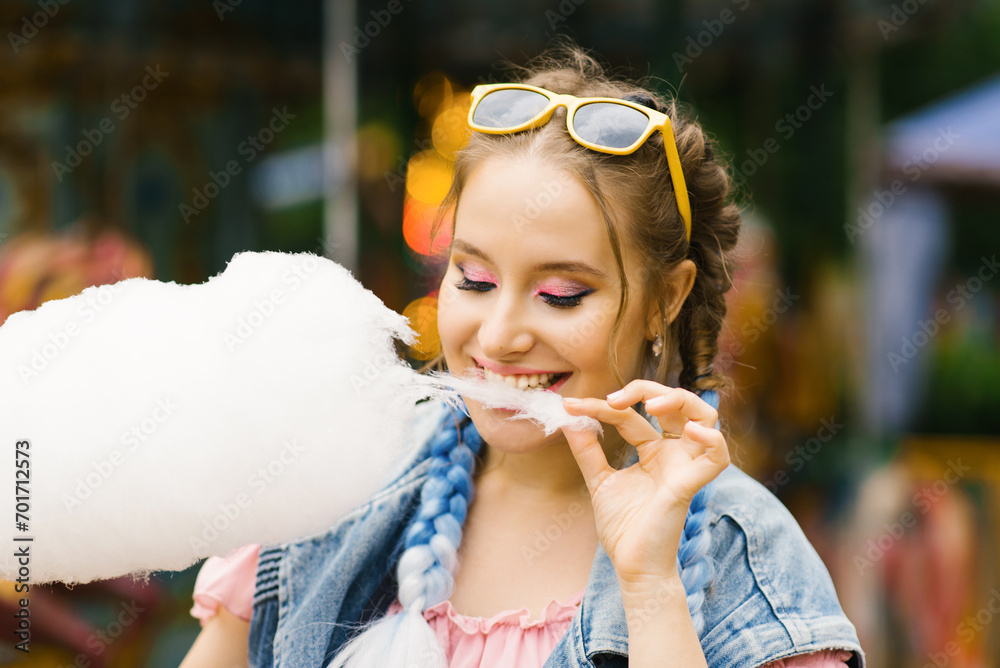 Funny young girl eats cotton candy on a sunny day at an amusement park Funny young girl eats cotton candy on a sunny day at an amusement park