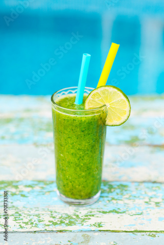 Freshly blended green fruit smoothie in glass with straw