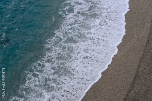 A view of a small wave breaking on the beach from above. Torre del Mare, Liguria, Italy - December 23, 2023.
