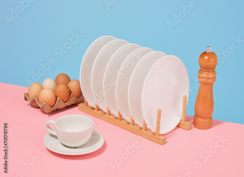 White plates stand in a wooden utensil stand. Chicken eggs, wooden pepper shaker and cup.