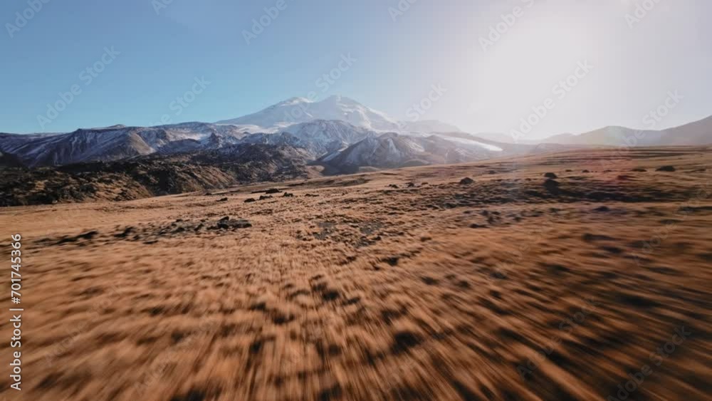 Low flight of a sports FPV drone at high speed high in the mountains over a yellow autumn field surrounded by snow-capped mountains of the Caucasus mountain range and Elbrus volcano