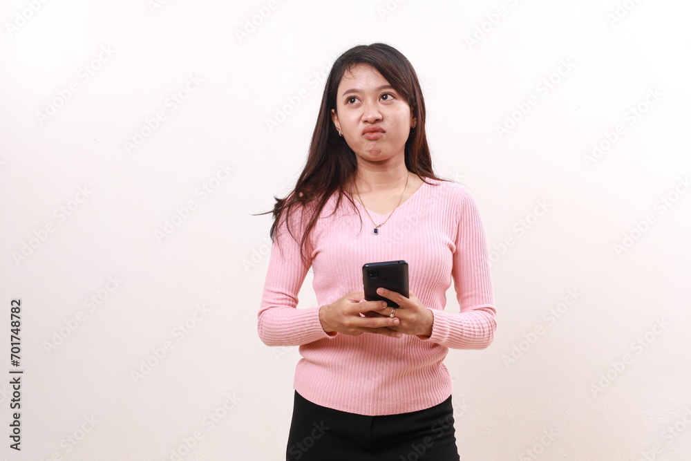 Unhappy young asian girl standing while holding a cell phone. Isolated on white background Unhappy young asian girl standing while holding a cell phone. Isolated on white background