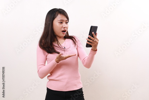 Shocked young asian girl standing while using a cell phone. Isolated on white background