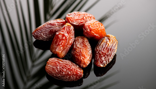 Dates fruit. Date fruits with palm tree leaf reflection on black background. Heap of Medjool dates close up. Tasty healthy Food