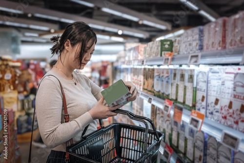 A young and beautiful Asian girl is shopping in a supermarket, picking fresh milk from the dairy shelves. She eats healthy, nutritious, and has a balanced diet and lifestyle photo