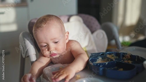 baby dirty eats. happy family a child toddler concept. baby dirty sitting messing with food at the table for feeding in the kitchen. lifestyle grimy toddler in the kitchen photo