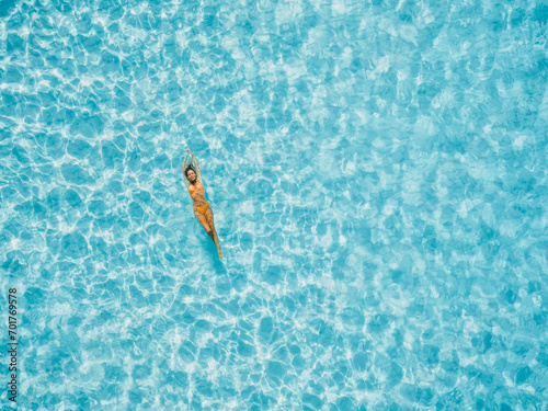 Woman floating in transparent blue ocean. Aerial view, top view.