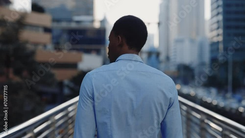 Back View of Young Successful African American Man in Shirt Walking Across Bridge in Business District. The Back of Businessman Walking Through the City on Way to Work. People Concept