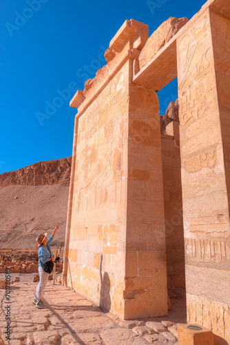 A woman looking at hieroglyphs - Hatshepsut Temple at sunrise in Valley of the Kings and red cliffs western bank of Nile river - Luxor- Egypt