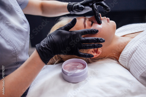 Close-up of a master applying silicone patches under the eyes of a pretty female blond client