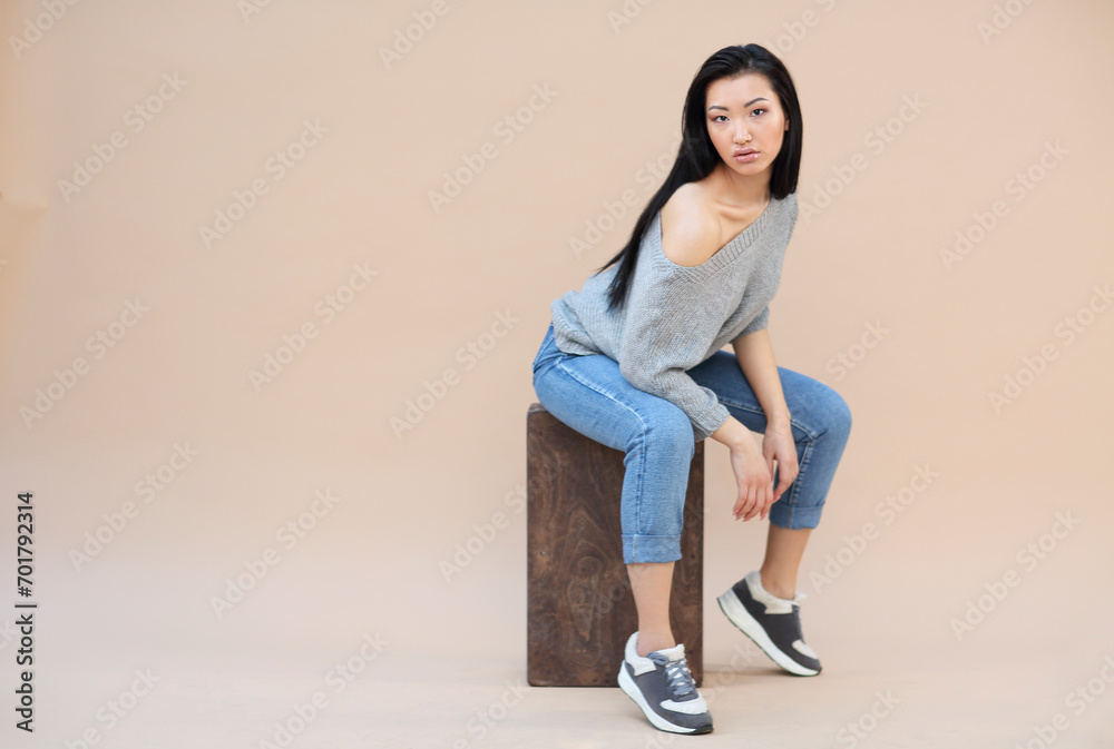 Beauty portrait of sensual asian young woman with dark long hair in cozy knitted grey sweater on the beige background Beauty portrait of sensual asian young woman with dark long hair in cozy knitted grey sweater on the beige background