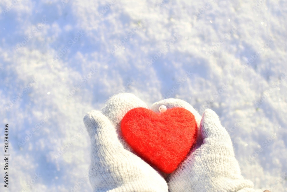 Women's hands in knitted mittens hold a heart. 