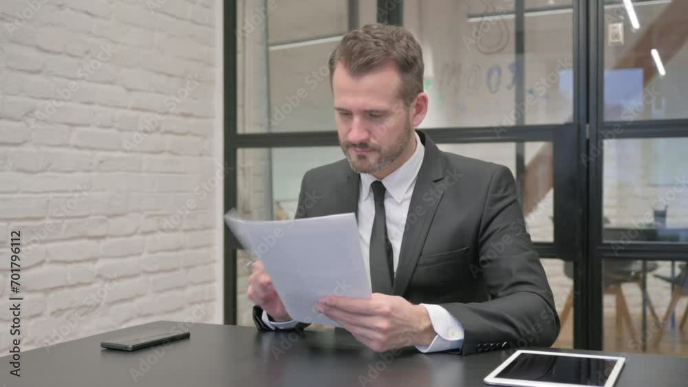 Middle Aged Businessman Celebrating while Reading Documents Middle Aged Businessman Celebrating while Reading Documents