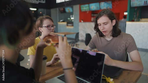 a group of students sit in a cafe and lifestyle do a project on a laptop together. business concept of modern training and development. students discuss their homework and eat fast food burgers photo