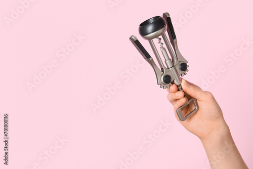Female hand holding wine opener on pink background photo