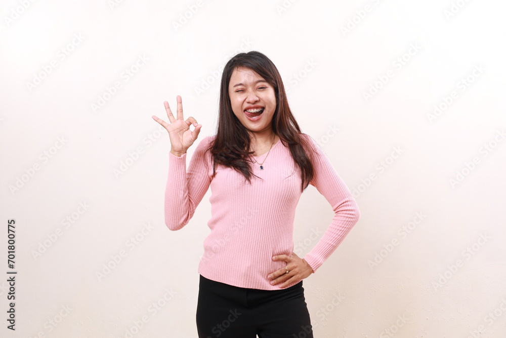 Happy carefree young asian girl standing while showing okay hand gesture. Isolated on white background