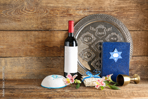 Composition with bottle of wine, Passover Seder plate, cup, Torah, kippah and flowers on wooden background