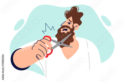 Unhappy man trims beard with scissors because of new dress code at work or appearance of lice