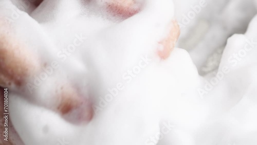 Female hands are washing with soap bubbles. Woman plays with fluffy foam in bathtub, macro. Lady holds handful of soap bubbles, close up.