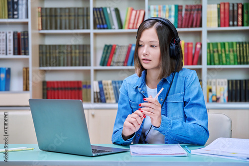 Female college student in headphones with laptop having online video chat, inside library