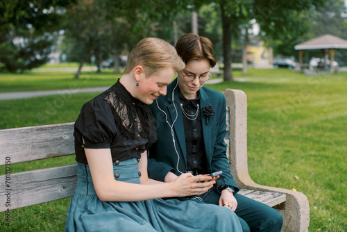 An LGBT couple looking happy while listening to music at a park before prom night.