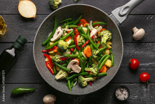 Frying pan with fresh vegetables on black wooden background photo