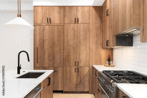 A kitchen detail with wood cabinets, black faucet, a bronze light fixture hanging above the white marble countertop, and a white subway tile backsplash.